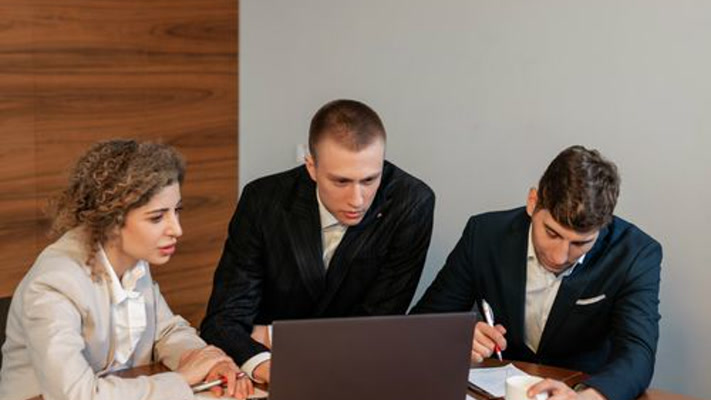 Three colleagues focus on a laptop during a workplace meeting.